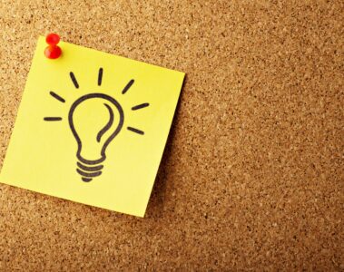 yellow post it note with cartoon drawing on a light bulb, on a tan cork boad
